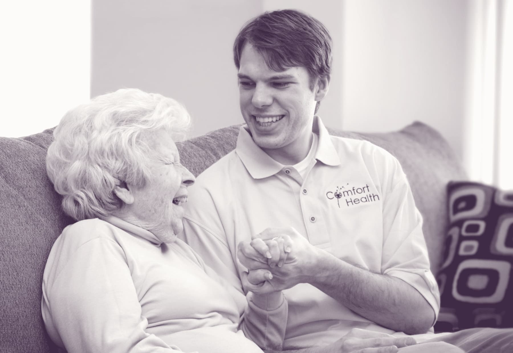 A Comfort Health caregiver and client laughing together, hands gently overlapping.
