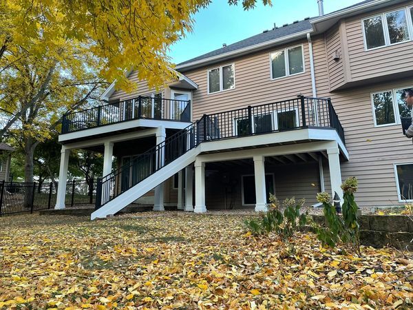 Eden Prairie back yard — Elevated cedar build with iron rail and white columns, photographed in fall. The leaves under the deck show the daylight clearance.