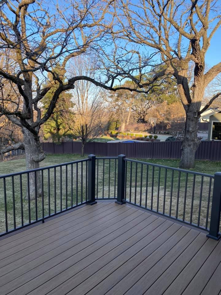 Edina back yard — Composite plank with iron picket rail, golden-hour light through bare oaks. A first-person view from the deck out into the yard.