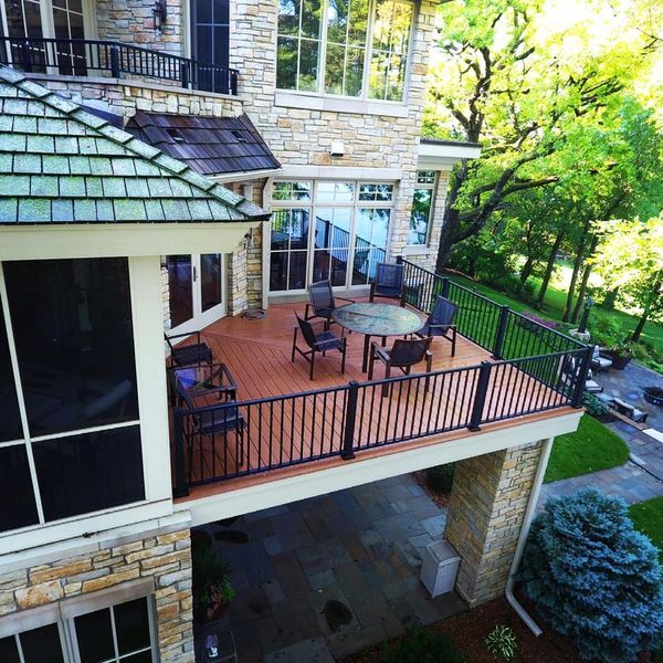 Lake Minnetonka — Multi-level cedar stepping down through stone columns to mature lakefront landscaping. Sunset light, cedar planks, iron rail.