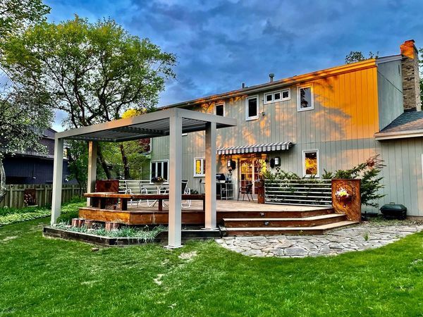 Cross Lake retreat — White-frame pergola with wood-clad ceiling and warm interior lighting at twilight. The yard turns into a room as the sun drops.